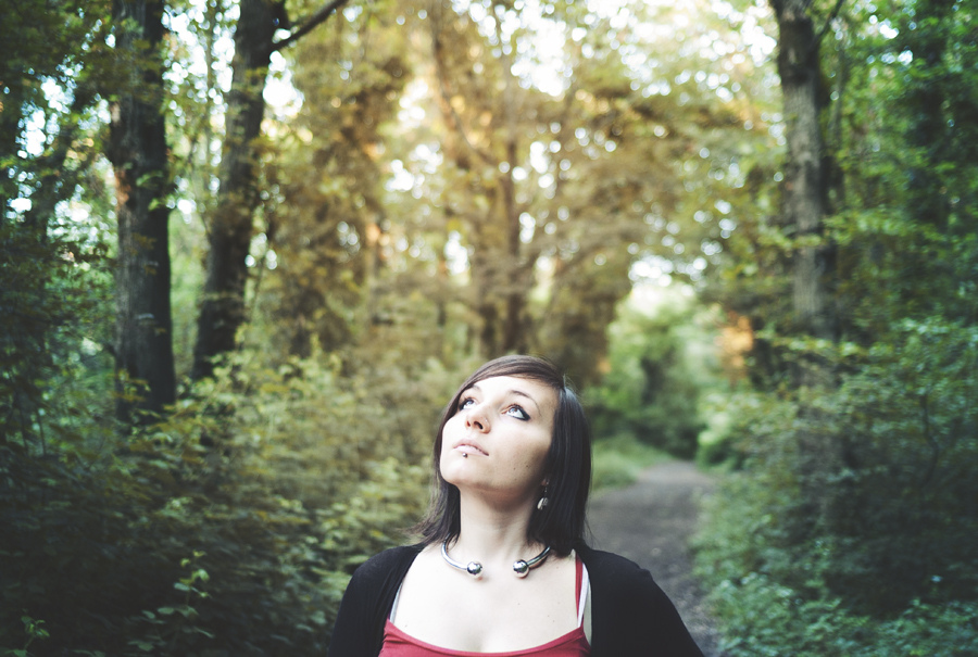 A woman in a red top standing in a wooded area.
