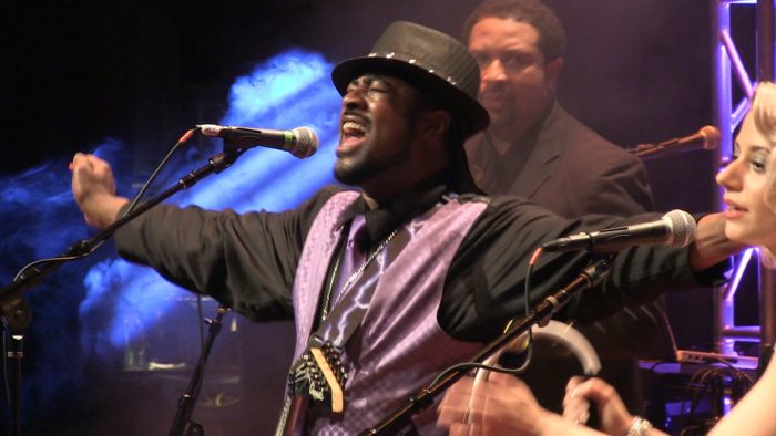 A man in purple shirt and hat playing guitar.