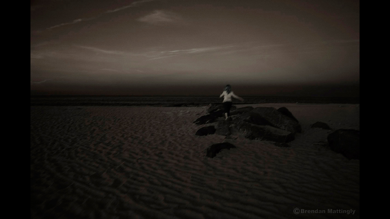 A woman is standing on a rock at the beach at night.