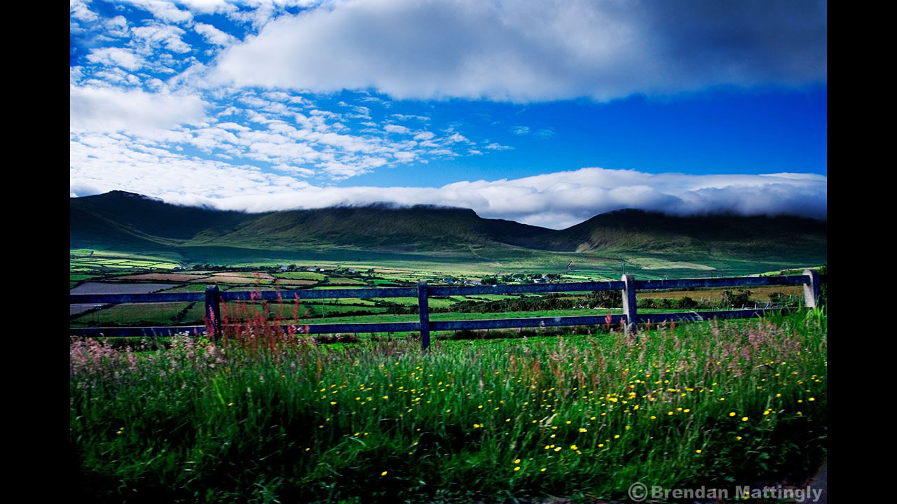 A grassy field with a fence and mountains in the background.