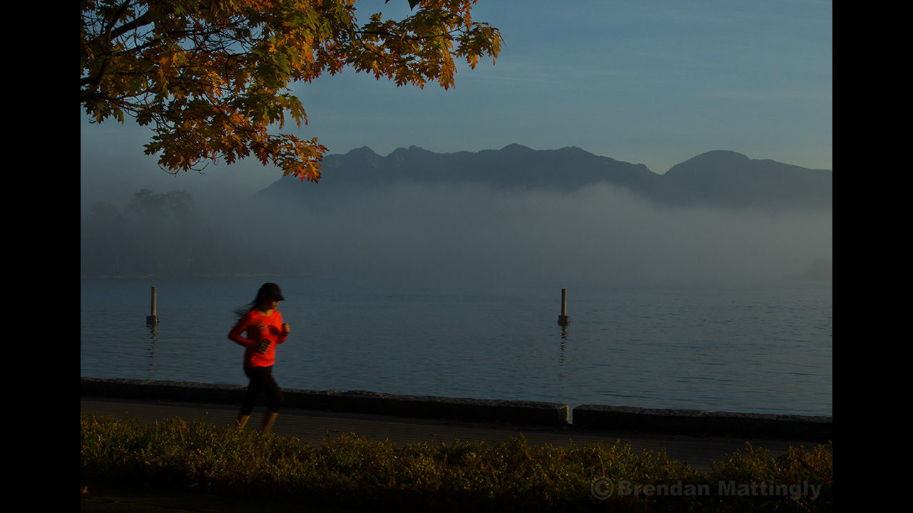 A woman jogging on a foggy morning near a lake.