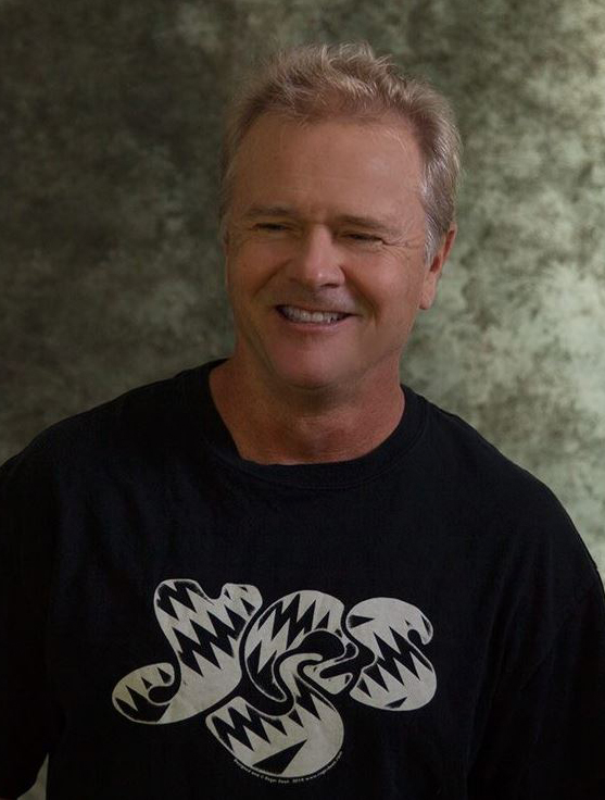 A man in a black tshirt smiling for the camera.