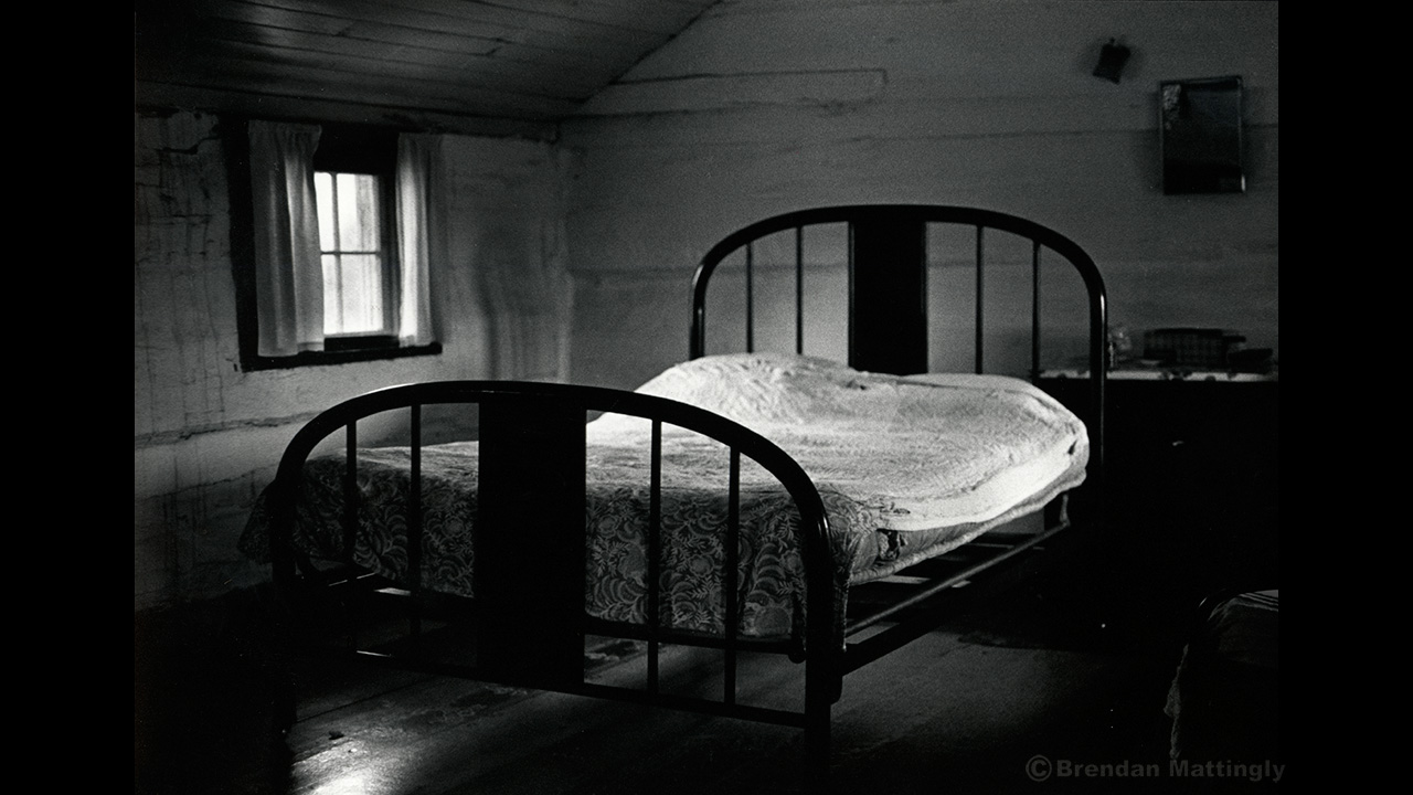 A black and white photograph of a bed in a room.
